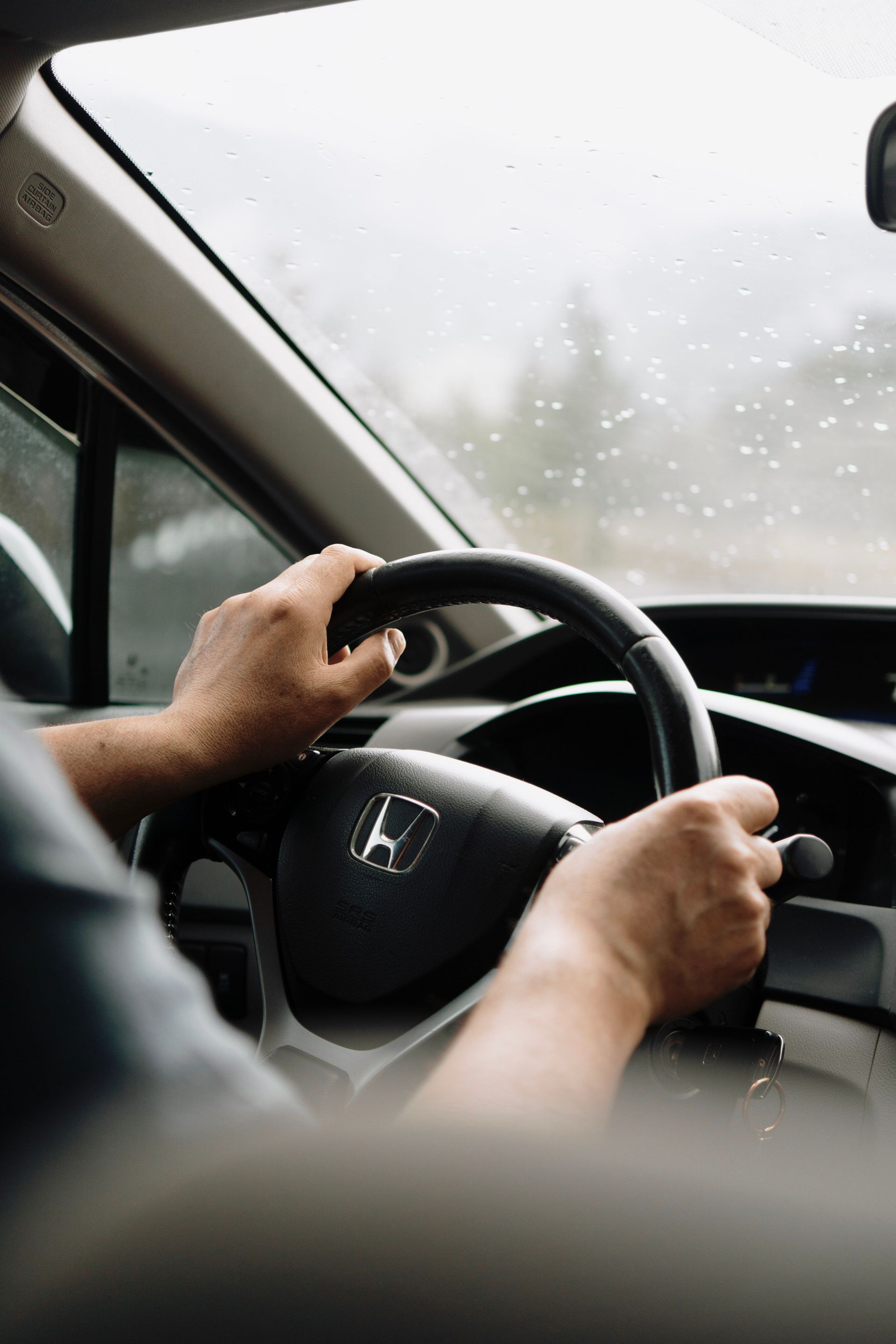A person drives a car through rainy weather, focusing on the road ahead.